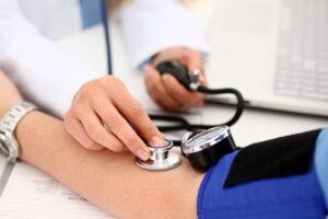 Focus is on a doctor taking a patient's blood pressure during a medical exam. Both parties are unidentifiable. 