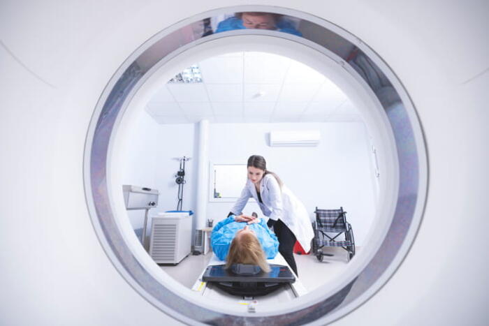 A Doctor Helping A Woman Get Ready On The Table Of A Ct Scan Before She Has Her Lungs Screened.